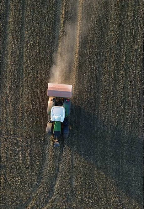 Aerial view of a tractor spreading fertilizer across a bare field